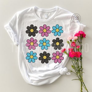 May include: White t-shirt with a pattern of nine glittery daisies in black, pink, and blue.