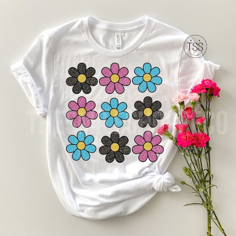 May include: White t-shirt with a pattern of nine glittery daisies in black, pink, and blue.