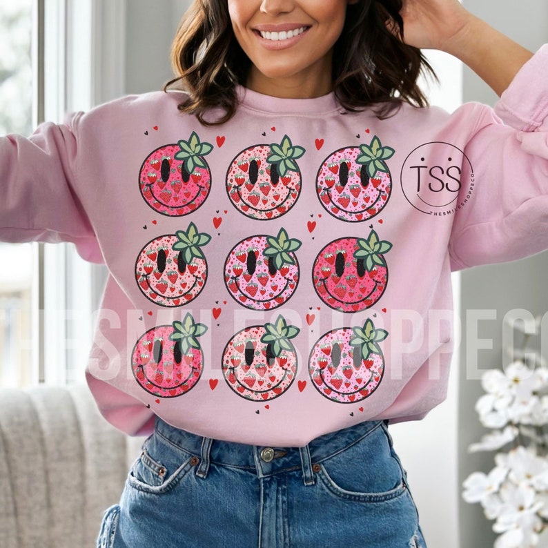May include: Pink sweatshirt with a graphic of nine smiling strawberry faces with hearts and leaves. The text "TSS" is on the right side of the sweatshirt.
