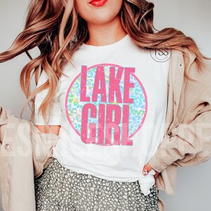 May include: White t-shirt with a pink circle graphic that says "LAKE GIRL" in pink letters. The circle has a blue and green leopard print pattern.