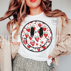 May include: White t-shirt with a black and white smiley face graphic. The smiley face is filled with a pattern of red strawberries and white hearts.