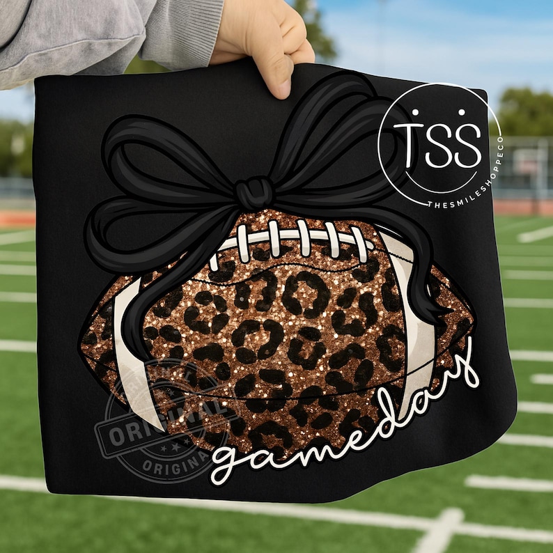 K&ouml;nnte beinhalten: Schwarzer Stoff mit einem Football-Design mit Leopardenmuster und einer schwarzen Schleife. Das Wort "gameday" ist in wei&szlig;er Schrift geschrieben. Das Bild wird vor einem gr&uuml;nen Feldhintergrund gehalten.