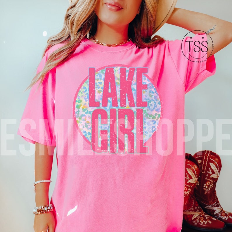 May include: Pink t-shirt with a circle graphic that says "LAKE GIRL" in pink letters with a distressed look. The circle graphic has a colorful leopard print pattern.