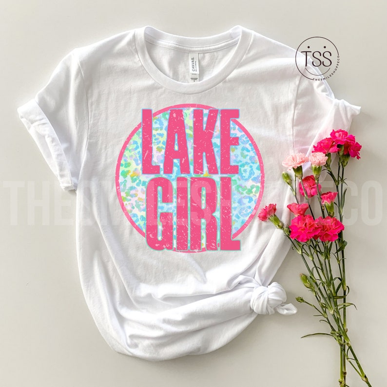 May include: White t-shirt with a pink circle graphic that says "LAKE GIRL" in pink letters. The circle has a blue, green, and pink leopard print pattern.