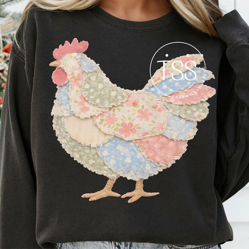 May include: Dark gray sweatshirt featuring a patchwork chicken design. The chicken has a pink comb and beak, with body sections in floral and striped patterns of pink, blue, and green. The sweatshirt has a crew neck.