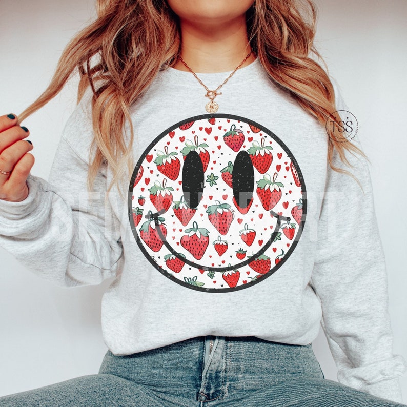 May include: A gray sweatshirt with a black and white smiley face design. The smiley face is filled with a pattern of red strawberries and white hearts.