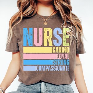 Op de afbeelding: Een bruin t-shirt met het woord "NURSE" in grote, kleurrijke letters. Daaronder staan de woorden "CARING", "LOYAL", "STRONG" en "COMPASSIONATE". Het shirt heeft een vintage, verweerde uitstraling.