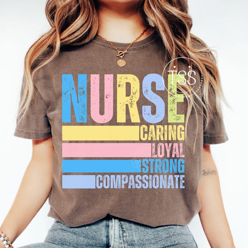 Op de afbeelding: Een bruin t-shirt met het woord "NURSE" in grote, kleurrijke letters. Daaronder staan de woorden "CARING", "LOYAL", "STRONG" en "COMPASSIONATE". Het shirt heeft een vintage, verweerde uitstraling.