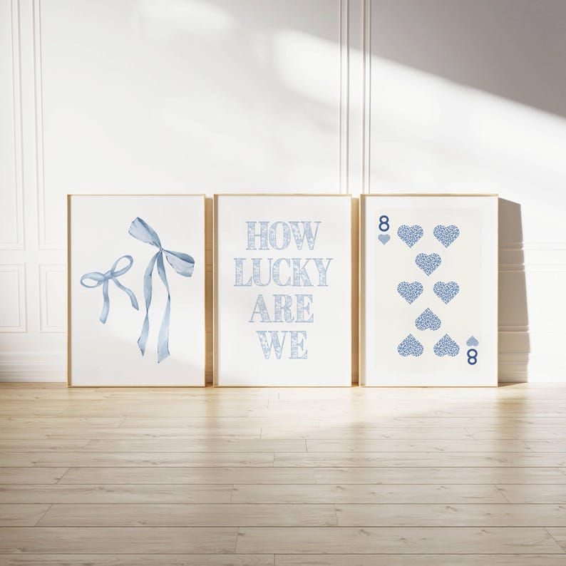 May include: Three framed art prints. The left print features a watercolor bow in light blue. The center print has the text "HOW LUCKY ARE WE" in light blue. The right print shows the eight of hearts playing card.