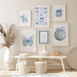 May include: A white bench with two white wicker baskets underneath. There are six framed prints on the wall above the bench. The prints feature blue watercolor illustrations of a butterfly, a balloon animal, a perfume bottle, a disco ball, and bows. The text "Lucky girl" is on one of the prints.