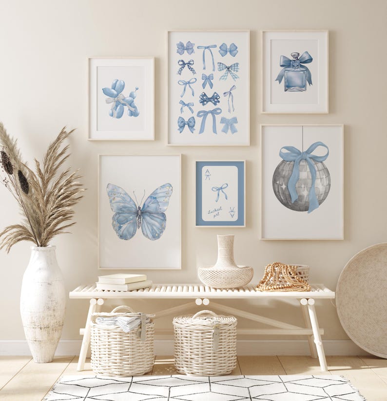 May include: A white bench with two white wicker baskets underneath. There are six framed prints on the wall above the bench. The prints feature blue watercolor illustrations of a butterfly, a balloon animal, a perfume bottle, a disco ball, and bows. The text "Lucky girl" is on one of the prints.