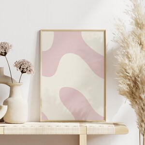 May include: A framed abstract print with pink and cream colored organic shapes. The print is displayed on a light wood shelf with two ceramic vases and dried flowers.