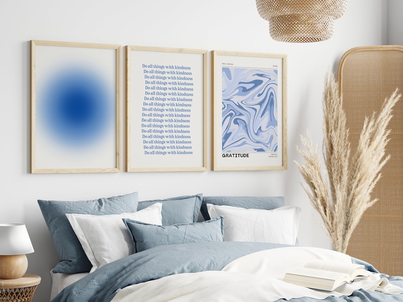 Op de afbeelding: Drie ingelijste prints op een witte muur boven een bed met blauwe beddengoed. De print aan de linkerkant is een blauwe gradi&euml;nt. De middelste print heeft de tekst "Do all things with kindness" 17 keer herhaald. De print aan de rechterkant heeft een blauw abstract ontwerp en de tekst "GRATITUDE".