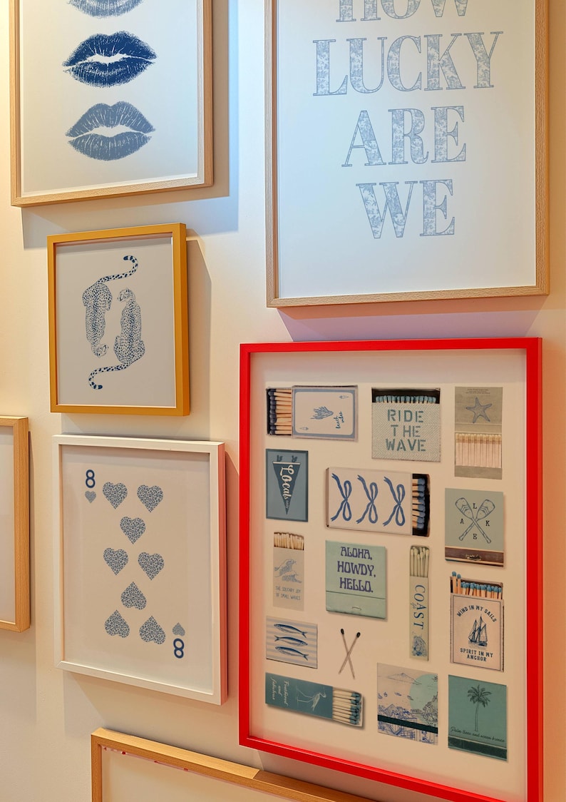 May include: A collection of framed art pieces with a variety of designs. The art includes blue lips, cheetahs, playing cards, and matchbox art with phrases like "Ride the Wave" and "Aloha, Howdy, Hello." The frames are in various colors, including red and gold.