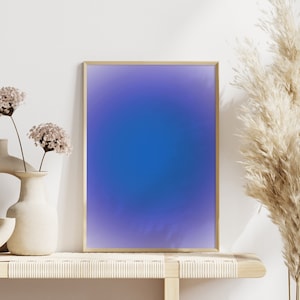 Peut inclure: Une impression abstraite encadr&eacute;e avec un d&eacute;grad&eacute; de couleurs violettes et bleues. L'impression est expos&eacute;e sur une &eacute;tag&egrave;re en bois clair avec deux vases de fleurs s&eacute;ch&eacute;es et une plante de gramin&eacute;es s&eacute;ch&eacute;es.