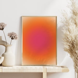 Peut inclure: Une impression abstraite encadr&eacute;e avec un d&eacute;grad&eacute; de couleurs orange, rose et rouge. L'impression est expos&eacute;e sur une &eacute;tag&egrave;re en bois clair avec deux vases et des fleurs s&eacute;ch&eacute;es.