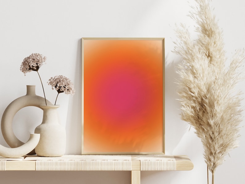 Peut inclure: Une impression abstraite encadr&eacute;e avec un d&eacute;grad&eacute; de couleurs orange, rose et rouge. L'impression est expos&eacute;e sur une &eacute;tag&egrave;re en bois clair avec deux vases et des fleurs s&eacute;ch&eacute;es.
