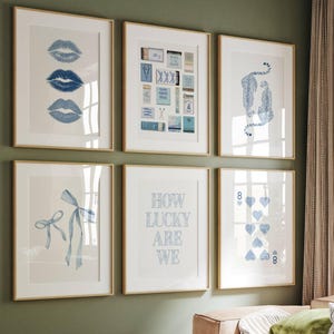 May include: Six framed art prints with gold-colored frames hang on a green wall. The prints feature blue illustrations of lips, matchboxes, leopards, a bow, the text "HOW LUCKY ARE WE", and playing card symbols.