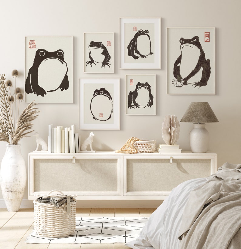 May include: A set of six black and white illustrations of frogs on a white background. The illustrations are framed and hung on a white wall above a white dresser with a white lamp on the right side of the dresser.