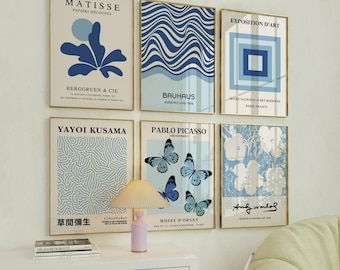 Op de afbeelding: Een verzameling van zes ingelijste kunstdrukken met gouden frames. De prints tonen verschillende abstracte ontwerpen, waaronder blauwe bloemen- en geometrische patronen en vlinderillustraties. De prints bevatten de namen van beroemde kunstenaars en kunstbewegingen.
