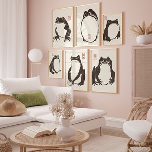 May include: A set of six black and white framed prints featuring stylized illustrations of frogs. The prints are hung on a light pink wall in a living room setting.