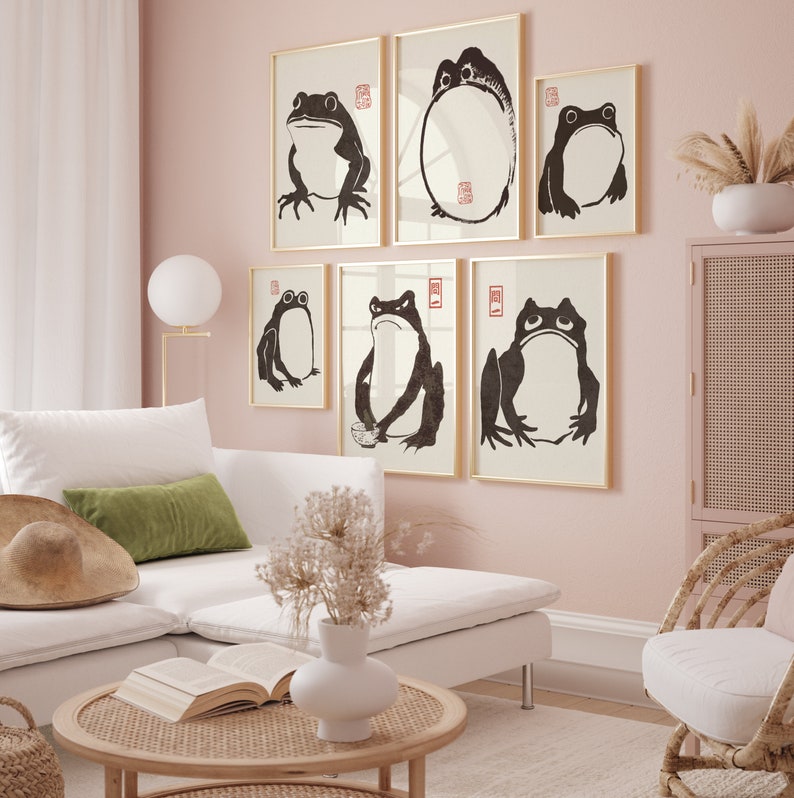 May include: A set of six black and white framed prints featuring stylized illustrations of frogs. The prints are hung on a light pink wall in a living room setting.