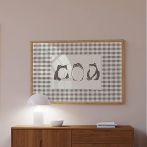 May include: A framed artwork featuring three stylized frog illustrations. The frogs are depicted in a minimalist style with varying poses, set against a gingham pattern background. The frame is a light wood color.
