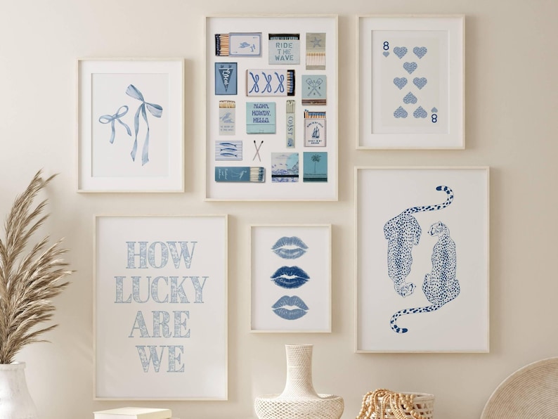 May include: A collection of framed art prints in shades of blue and white. The prints feature various designs, including bows, playing cards, matchbox art, lips, and cheetahs. The phrase "HOW LUCKY ARE WE" is also displayed.