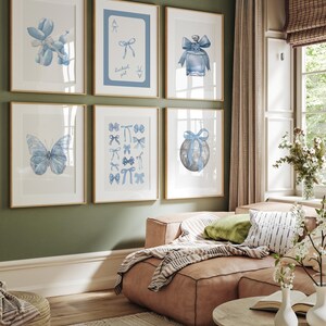 May include: A set of six framed prints with blue and white watercolor illustrations of bows, butterflies, a balloon animal, a perfume bottle, and a globe. The frames are all light wood and the prints are arranged in a grid pattern on a green wall.