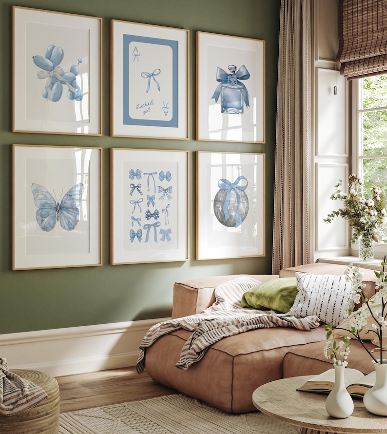 May include: A set of six framed prints with blue and white watercolor illustrations of bows, butterflies, a balloon animal, a perfume bottle, and a globe. The frames are all light wood and the prints are arranged in a grid pattern on a green wall.