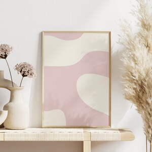 May include: A framed abstract print with pink and cream colored organic shapes. The print is on a shelf with two vases of dried flowers and a tall dried pampas grass.