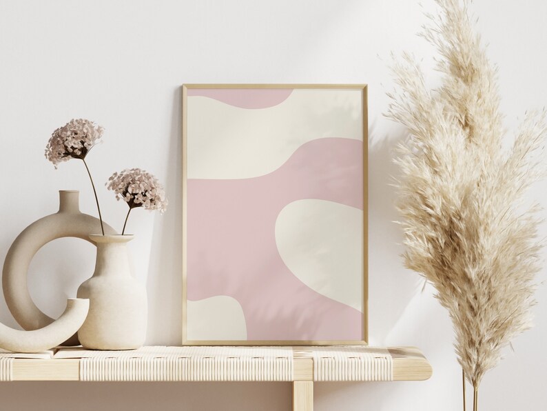 May include: A framed abstract print with pink and cream colored organic shapes. The print is on a shelf with two vases of dried flowers and a tall dried pampas grass.
