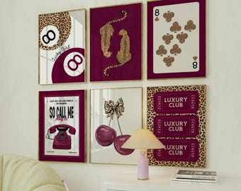 Op de afbeelding: Een verzameling ingelijste wandkunst met gouden randen. De kunstwerken tonen diverse ontwerpen, waaronder een poolbal, speelkaart, luipaardprint, kersen en een draaischijftelefoon. Het kleurenschema omvat bordeauxrood, wit en luipaardprint.