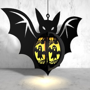 May include: A black metal bat silhouette with a yellow and orange sphere hanging from it. The sphere has a spiderweb design and three ghost figures inside.
