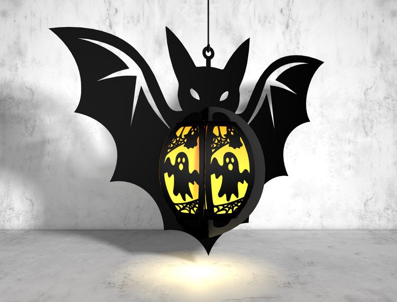 May include: A black metal bat silhouette with a yellow and orange sphere hanging from it. The sphere has a spiderweb design and three ghost figures inside.