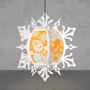 May include: A white paper snowflake-shaped pendant lamp with an orange interior. The lamp features cut-out designs of a snowman, snowflakes, and a winter landscape. The lamp is suspended from a black cord against a gray background.
