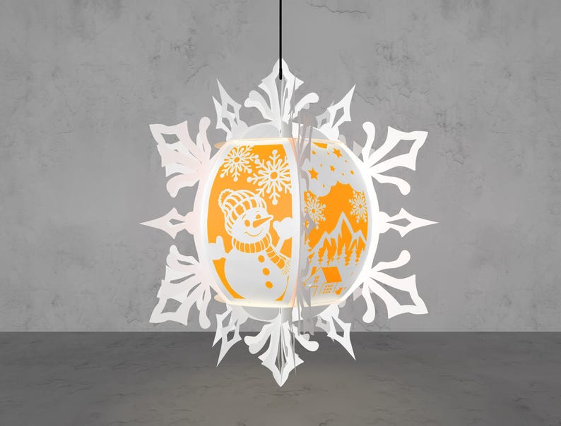 May include: A white paper snowflake-shaped pendant lamp with an orange interior. The lamp features cut-out designs of a snowman, snowflakes, and a winter landscape. The lamp is suspended from a black cord against a gray background.