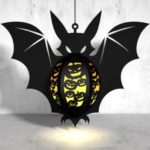 May include: A black bat silhouette with a hanging, round, orange and yellow pumpkin-shaped lantern. The lantern has a black outline and is filled with smaller pumpkin faces.
