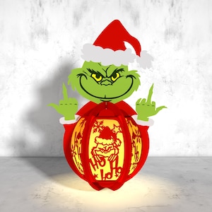 May include: A green Grinch character wearing a red Santa hat and holding a red Christmas bauble with a white snowflake design and the text "Merry Ho Ho".