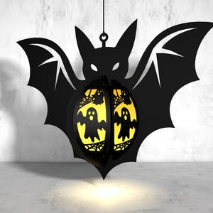 May include: A black bat-shaped Halloween lantern with a yellow, translucent, ghost-shaped design. The lantern is hanging from a string.