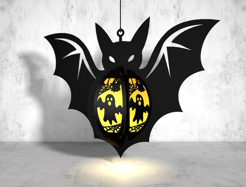May include: A black bat-shaped Halloween lantern with a yellow, translucent, ghost-shaped design. The lantern is hanging from a string.