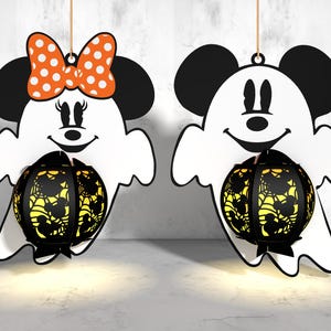 Peut inclure: Deux ornements de fantômes blancs avec des yeux et des bouches noirs, l'un avec un nœud rouge et blanc à pois et l'autre avec des oreilles noires. Les deux tiennent une lanterne en forme de citrouille noire et jaune avec un motif de toile d'araignée.