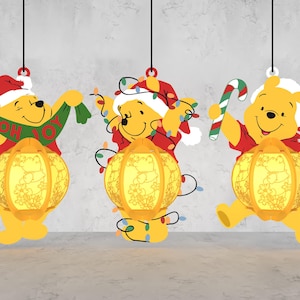 May include: Three yellow Winnie the Pooh Christmas decorations. Each decoration features Pooh Bear in a Santa hat and holding festive items like a candy cane, lights, and a scarf that says "OH JOY". Each decoration has a glowing lantern.