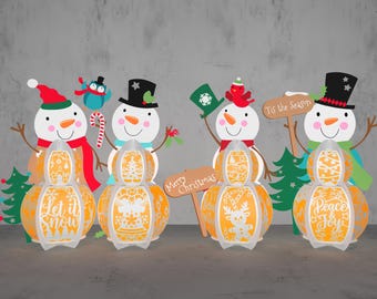 May include: Four snowman-shaped light-up decorations with different designs. The snowmen are made of white paper with orange, red, and green accents. The snowmen are holding signs that say "Let it snow", "Merry Christmas", "Tis the Season", and "Peace & Joy".