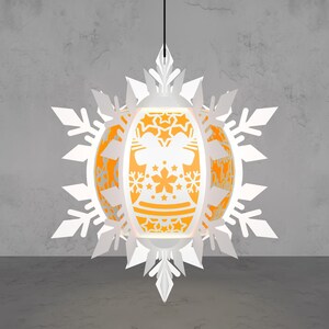 May include: A white paper lantern with an orange interior, featuring a snowflake design and intricate cut-out patterns. The lantern is suspended from a black cord, creating a festive and decorative lighting element.