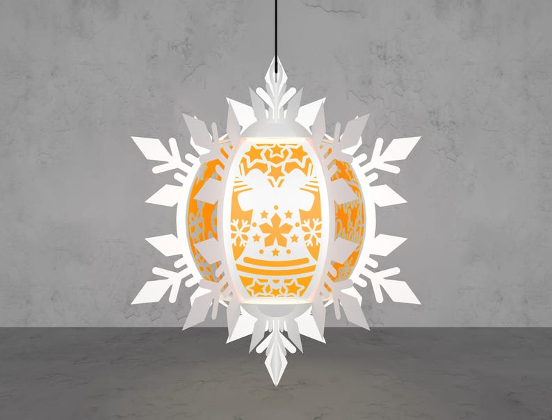 May include: A white paper lantern with an orange interior, featuring a snowflake design and intricate cut-out patterns. The lantern is suspended from a black cord, creating a festive and decorative lighting element.