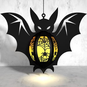 May include: A black bat-shaped Halloween lantern with a yellow and orange spiderweb design. The lantern is hanging from a string and has a light inside.