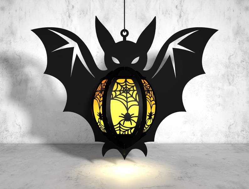May include: A black bat-shaped Halloween lantern with a yellow and orange spiderweb design. The lantern is hanging from a string and has a light inside.