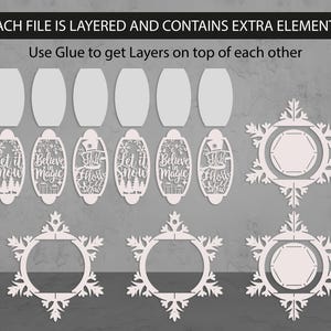 May include: White laser-cut Christmas ornaments and snowflake designs. The image includes oval-shaped ornaments with phrases like "Let it Snow" and "Believe in Magic". The text "EACH FILE IS LAYERED AND CONTAINS EXTRA ELEMENTS" is at the top.