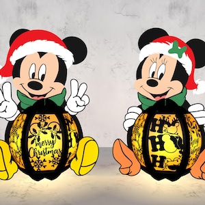 Könnte beinhalten: Zwei Weihnachtslaternen mit Mickey und Minnie Mouse. Mickey trägt einen Weihnachtsmannhut und einen grünen Schal und zeigt das Friedenszeichen. Minnie trägt einen Weihnachtsmannhut mit einer grünen Schleife. Die Laternen sind schwarz mit gelbem Licht und tragen die Aufschrift "Merry Christmas" und "Ho Ho Ho".